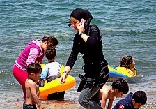 Strandszene ungewohnt: Frauen begeben sich in voller Kleidung ins Wasser. Mnner und Kinder baden, mit dem , was sie gerade an haben.